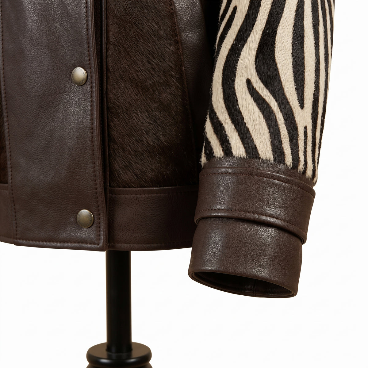 Close-up of a jacket sleeve and side panel showing dark brown leather, dark brown hair-on-hide, and a zebra-print fabric section on a white background.