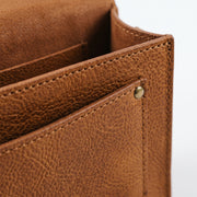 "Extreme close-up of the interior pocket compartment on a tan leather crossbody bag, showing the leather grain texture, stitching, and a brass rivet."