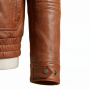 "Close-up detail of a tan brown leather bomber jacket's cuff, showing snap button closure and stitched leather grain texture."