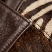 Close-up detail of a brown leather trim with contrast stitching, attached to a brown and beige cowhide material.