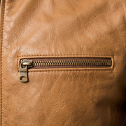 "Close-up of a bronze zipper pocket on a tan leather biker jacket, showing the zipper pull and natural leather grain texture."