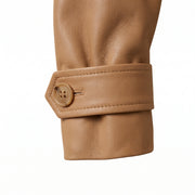 "Close-up detail of a tan leather trench coat's cuff with a button strap closure."