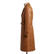 "Full-length side profile view of the tan leather trench coat on a mannequin, showing the collar, waist belt, flap pocket, and cuff strap silhouette against a white background."