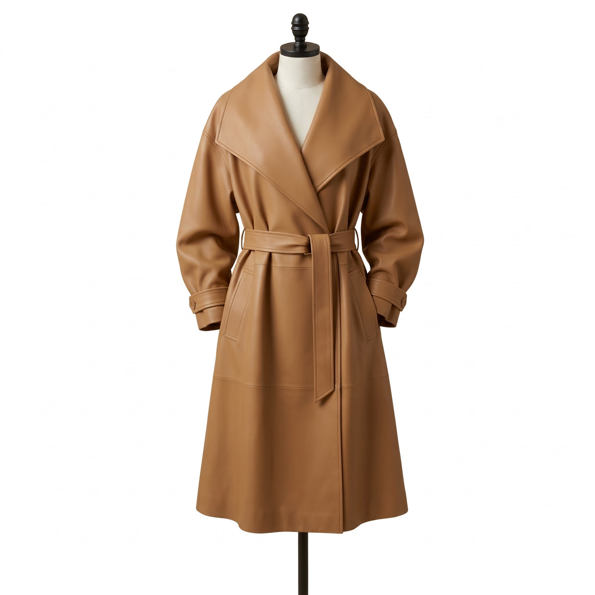"Front view of a tan leather trench coat with an oversized shawl collar, tied belt, and flap pockets, displayed on a mannequin against a white background."