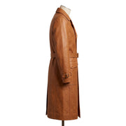 "Opposite side profile view of the tan leather trench coat on a mannequin, showing the collar, waist belt, flap pocket, and cuff strap silhouette against a white background."