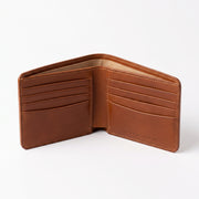 Open tan brown leather bifold wallet interior shown at an angle, featuring empty multiple card slots on both sides with visible cream stitching, a beige fabric lining along the top edge, and embossed text on the right panel reading 'Genuine Leather - Handmade in USA', photographed against a plain white background with soft shadow."