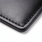 "Close-up of black leather wallet corner showing texture and hand stitching detail."