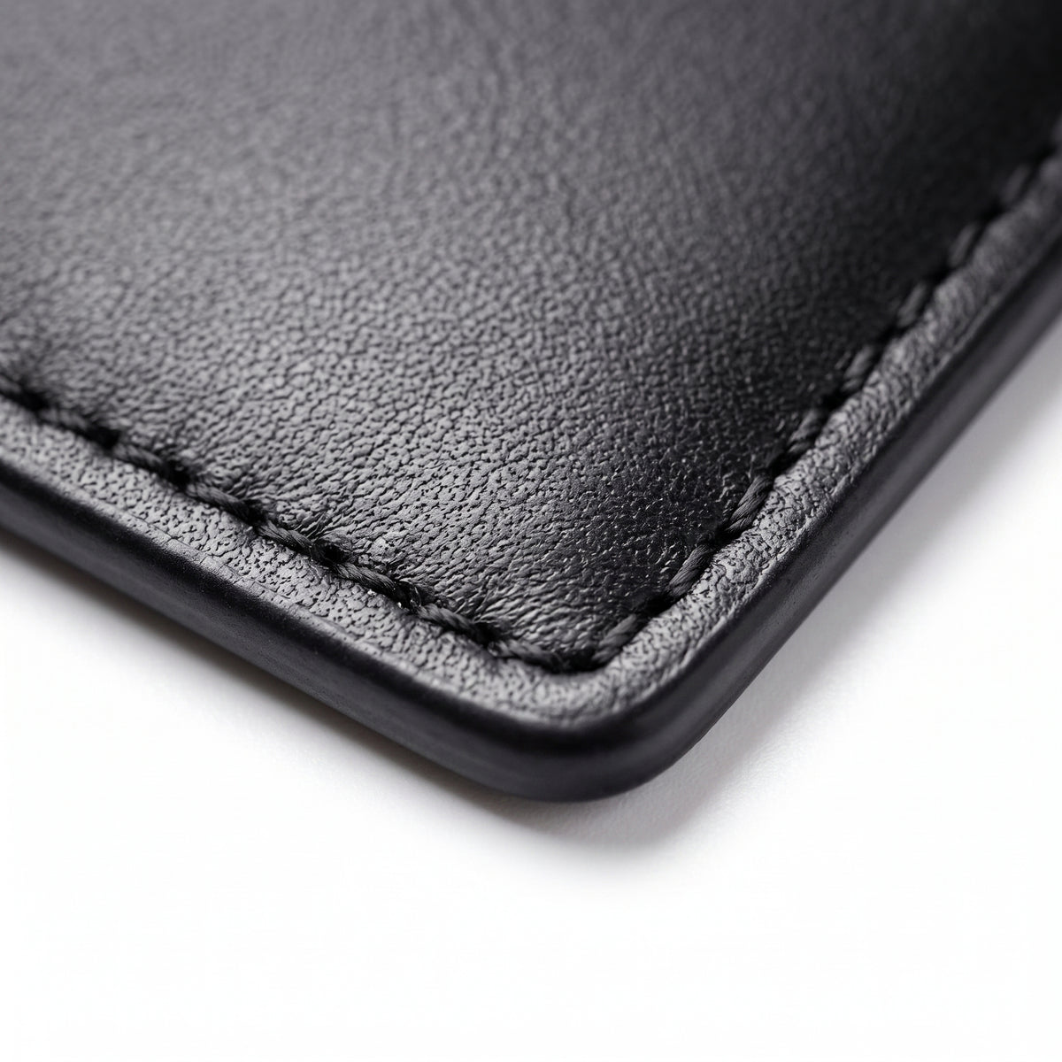 "Close-up of black leather wallet corner showing texture and hand stitching detail."