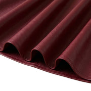 "Close-up of the rippled hemline of a maroon faux leather skirt, showing flowing folds and stitched edge detail against a white background."