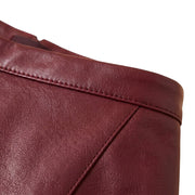"Extreme close-up of a maroon faux leather skirt's waistband, showing fine grain texture and stitched seam detail against a white background."