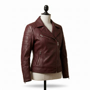 "Angled view of a maroon leather biker jacket with asymmetric front zipper, notch lapel, multiple zip pockets, and stud detailing, displayed on a mannequin against a white background."
