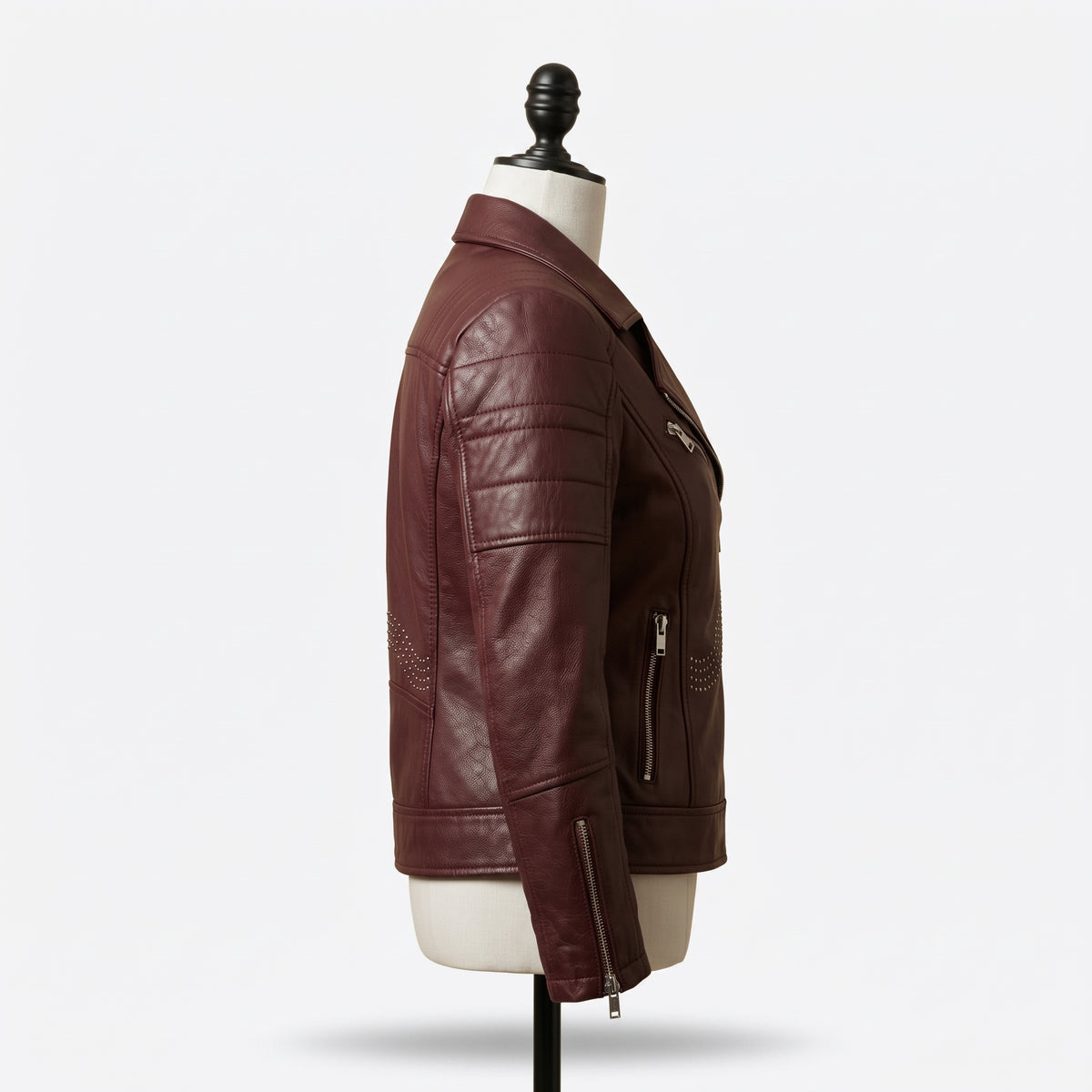"Full profile side view of a maroon leather biker jacket with notch lapel, zip pockets, and stud detailing, displayed on a mannequin against a white background."