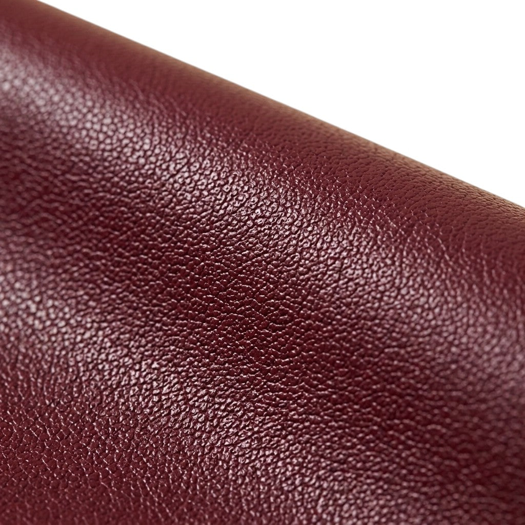 "Extreme close-up macro shot of maroon faux leather grain texture, showing fine pebbled surface detail against a white background."
