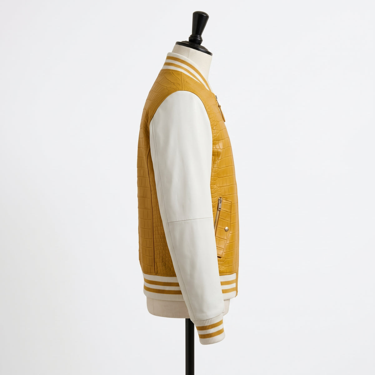 A side-profile view of a varsity-style jacket displayed on a mannequin against a plain white background. The jacket has a textured mustard yellow body with contrasting smooth off-white sleeves and striped ribbed trim.