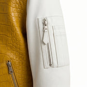 Close-up detail of a jacket showing a white faux-leather sleeve with a zippered pocket and a mustard yellow crocodile-embossed leather panel with a silver zipper.