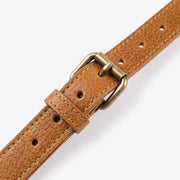 Close-up of the adjustable strap on a tan leather crossbody bag, showing the brass buckle, adjustment holes, and double-stitched leather texture."