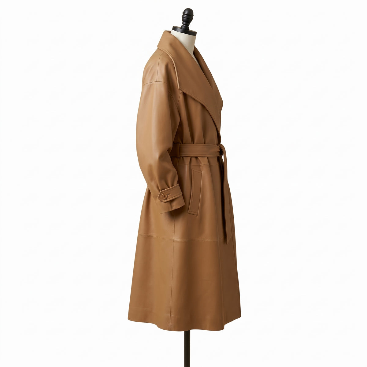 "Full profile side view of a tan leather trench coat with an oversized shawl collar, tied belt, and flap pocket, displayed on a mannequin against a white background."
