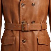 "Close-up of the torso area on a tan leather trench coat, showing double-breasted horn buttons, the waist belt with brass buckle, and flap pockets in detail."
