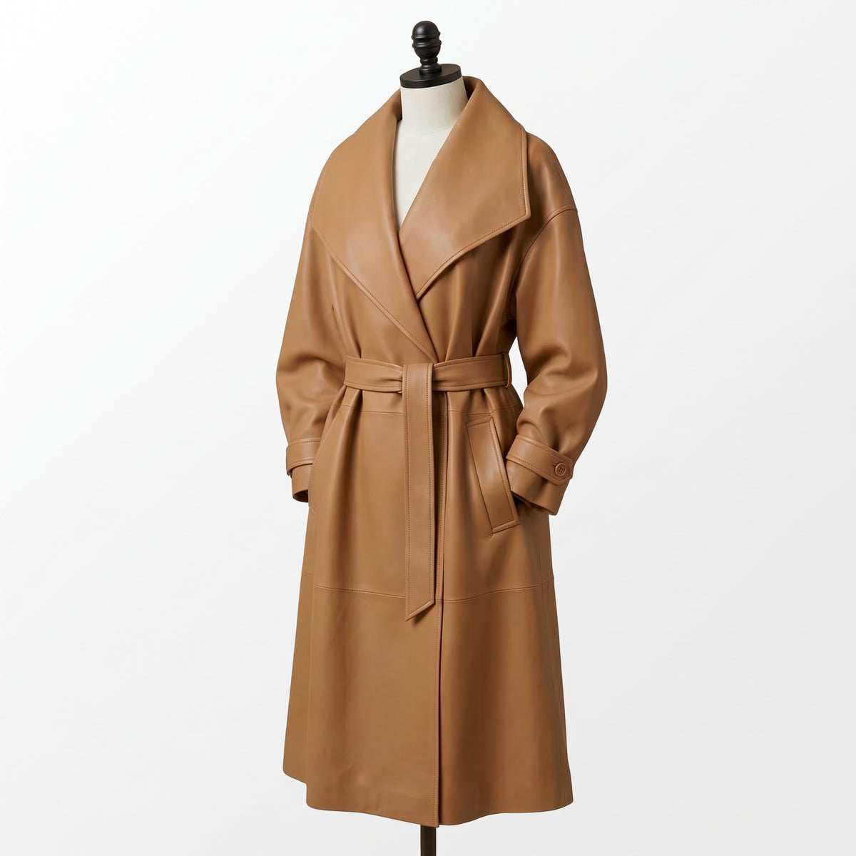 "Angled view of a tan leather trench coat with an oversized shawl collar, tied belt, and flap pockets, displayed on a mannequin against a white background."
