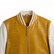 A close-up of a varsity-style jacket featuring a mustard yellow crocodile-embossed leather front with white sleeves and a striped ribbed collar.
