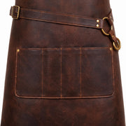 "Close-up detail of a dark brown leather apron's waist area, showing an adjustable diagonal strap with brass buckle and D-ring hardware, and a wide multi-compartment lower pocket with brass rivets and contrast tan stitching."