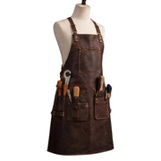 "Front angled view of a dark brown leather work apron displayed on a fabric mannequin, featuring adjustable neck straps, a zippered chest pocket, and multiple front tool pockets holding various tools including a wrench, chisels, wooden-handled hand tools, and a screwdriver, photographed against a plain white background."