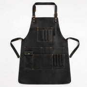 "Flat lay of black leather apron showing full shape, waist ties, and multiple pockets with brass hardware."