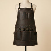 Front view of dark brown leather woodworking apron on mannequin with adjustable shoulder straps, chest pocket, tool loops and large utility pockets.