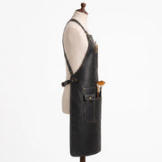 "Side profile of black leather apron with crossback straps and pockets holding paintbrushes."