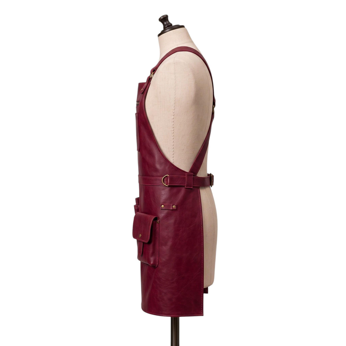 "Side profile view of a burgundy leather apron showing the strap, waist buckle, and a snap-flap pocket." 