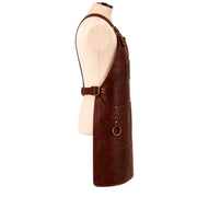 "Full side profile view of a brown leather work apron on a mannequin, showing the neck strap buckle, a slim pen pocket, adjustable waist buckle strap, a brass D-ring, and a lower front pocket with stitched edges."
