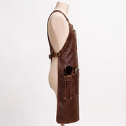 "Side view of brown leather barber apron on mannequin, showing pockets with scissors, comb, brush, and clippers."