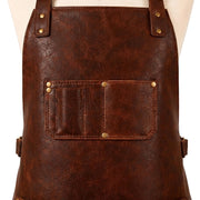 "Close-up of a brown leather apron's upper chest area, showing riveted shoulder strap attachments, a chest pocket with a pen slot and card compartment, and adjustable side buckle straps."