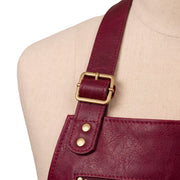 "Close-up of a burgundy leather apron's brass buckle and shoulder strap hardware."