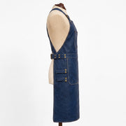 "Profile view of navy blue leather apron on a mannequin, showing the deep armhole cut, side chest pocket, adjustable waist belt with brass buckle, and a lower pocket with two side tool loops."