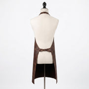 "Back view of a brown leather apron with crossed waist straps, displayed on a mannequin."