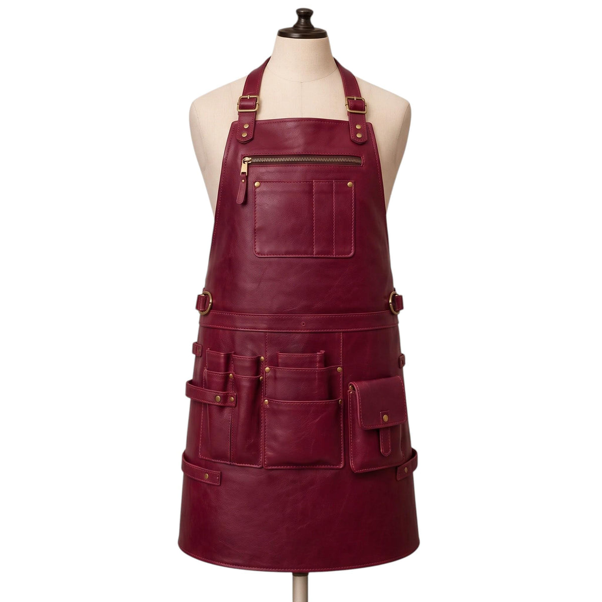 "Burgundy leather work apron with brass buckles, multiple tool pockets, and a zippered chest pocket, displayed on a mannequin."
