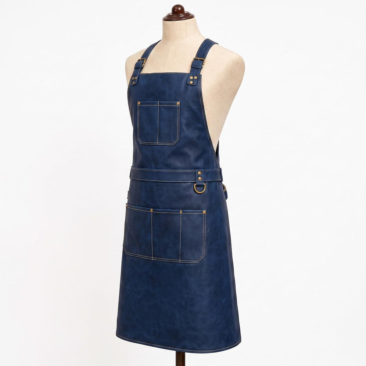 "Alternate side-angle view of navy blue leather apron on a mannequin, displaying brass buckle shoulder straps, a top chest pocket, a waist belt with D-ring hardware, and a lower pocket with tool loops on both sides."