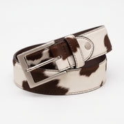 "Close-up angled view of a white and brown cow-print calf hair leather belt coiled to display a brushed silver-tone square buckle and stitching detail against a white background."