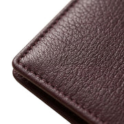 "Closed burgundy leather bifold wallet shown at an angle with a currency note peeking out from the side, on a white background.")