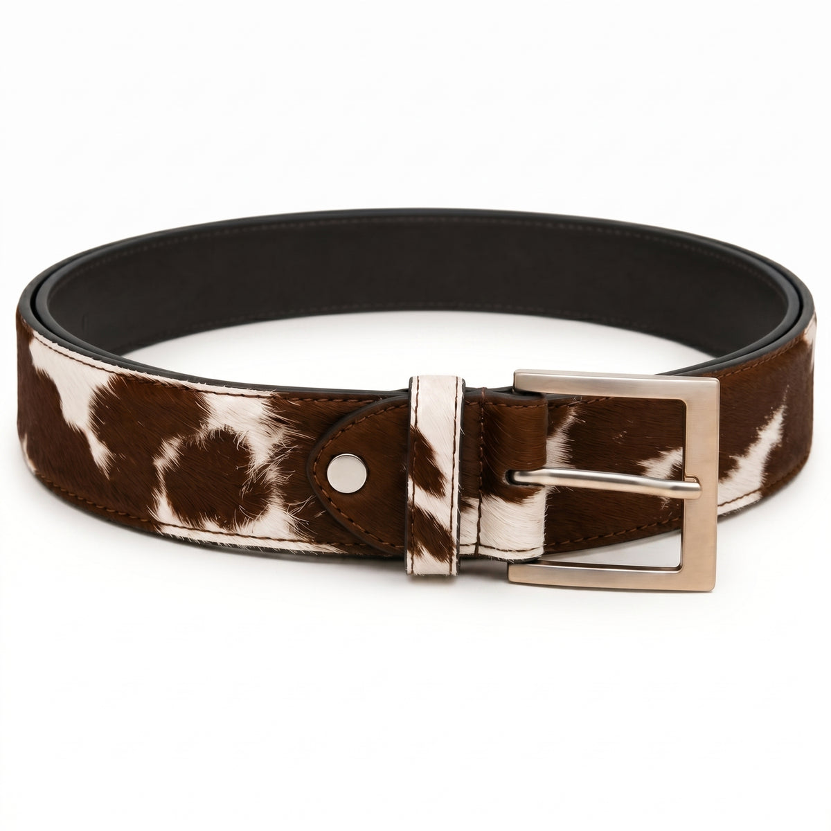 : "Brown and white cow-print calf hair leather belt formed into a circular loop, showing a brushed silver-tone square buckle and dark leather interior, photographed on a white background."