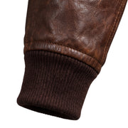 "Close-up of the sleeve cuff on a dark brown distressed leather bomber jacket, showing the leather texture and ribbed knit cuff detail."