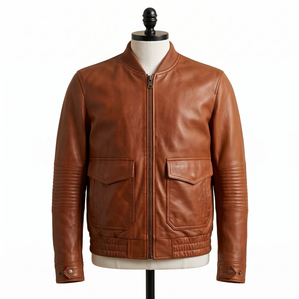 "Front view of a tan brown leather bomber jacket with ribbed collar, front zipper, flap pockets, and quilted elbow panels, displayed on a mannequin against a white background."